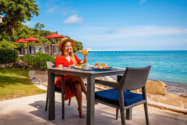 Stock image Vacation girl in luxury resort enjoys morning breakfast with fresh food and tropical sea view. Happy young woman on beachfront dining. Travel, vacation, summer holidays concept