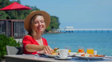 Yaz tatilinde olan mutlu bir kız yemek dolu tabaklarla dolu bir restoranda masada oturuyor. Seyahat eden bir kadın lüks bir tatil köyünde açık büfenin tadını çıkarırken güzel deniz manzarasının tadını çıkarıyor..