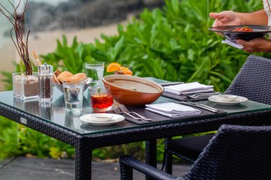 Sahil kenarındaki bir restoranda bir garson, misafirlerin özel günleri kutlayabileceği ya da arka planda çarpıcı bir deniz manzarası olan hafta sonu yemeğinin tadını çıkarabileceği bir masaya katılır..
