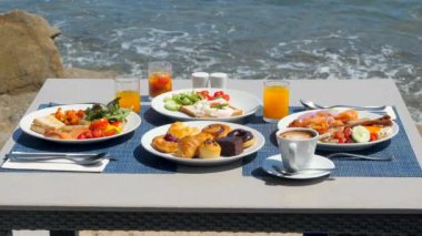 Masaya yayılmış lüks kahvaltı ve çarpıcı bir tropikal deniz manzarası ve dalgalar. Taze ve lezzetli yemekler, yaz tatilinde sabah yemeği. Seyahat, Tayland tatili konsepti