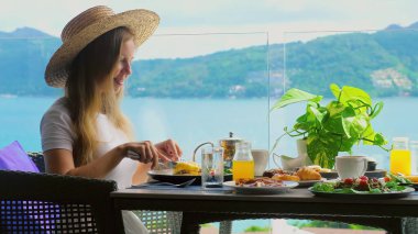 Deniz manzaralı bir kafede dinlenen, salata ve yumurta gibi taze sağlıklı yiyecekler yiyen bir kadın. Yaz tatillerinde Tayland, Asya 'daki tropik Phuket Adası' nda otel kahvaltısının tadını çıkarıyorum..