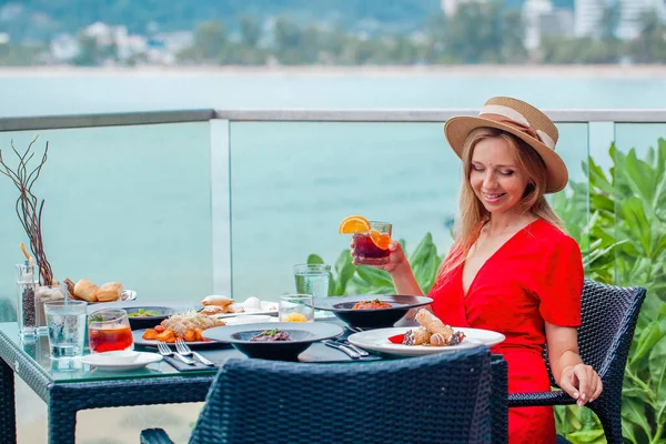 휴가를 즐기는 아름다운 여자가 알코올음료와 맛있는 식사를 있습니다 해변에 식당에서 — 스톡 사진