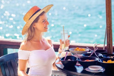 Yaz tatilindeki genç bir kadın deniz manzaralı lüks bir otel odasında lezzetli bir kahvaltı yapıyor. Kız yaz tatilinin tadını çıkarıyor..