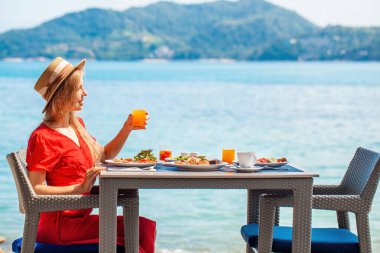 Kadın lüks bir otelde rahatlıyor, deniz manzarasının tadını çıkarıyor. Dişi gezgin, turkuaz okyanuslu tropik bir plajda, bir tatil yerinde sağlıklı bir kahvaltı yapar. Tayland tatili.