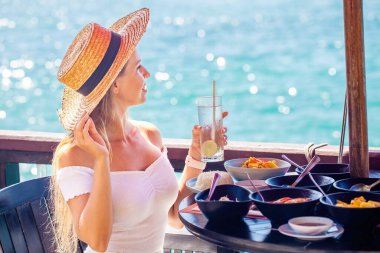 Yaz tatilindeki genç bir kadın deniz manzaralı lüks bir otel odasında lezzetli bir kahvaltı yapıyor. Kız yaz tatilinin tadını çıkarıyor..