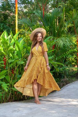 Parlak yaz elbisesi içindeki çekici beyaz kadın palmiye ağacının yanında dururken neşeyle gülümsüyor. Lüks tatil, kaygısız tatil..