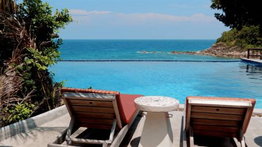 Plaj sandalyeleri ve deniz manzaralı köpüklü bir havuzun yanında bir masa. Tatil köyünde güneşli güzel bir gün. Boş zaman ve rahatlama kavramı.