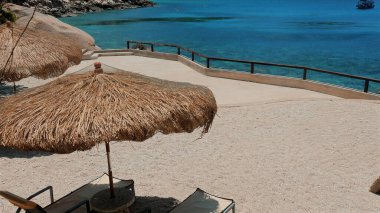 Akdeniz plajında iyi günler. Tropik tatil köyünde plaj sandalyesi ve şemsiyeler. Temiz mavi su ve kumlu sahilde güneşlenme. Bereketli yeşil dağlar. Dinlenmek ve güneşi emmek için mükemmel bir yer..