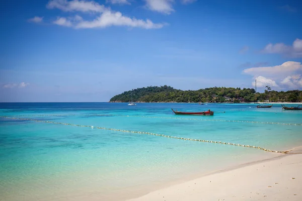 stock image Tropical beach with turquoise water and traditional Thai boat. Clear blue sky, white sandy shore, and idyllic scenery. Concept of serene relaxation and tropical paradise.