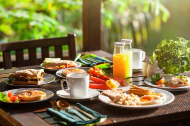 Tayland tatil köyündeki huzurlu gölün yanında nefis bir kahvaltı. Sandviç, salata ve taze sıkılmış portakal suyu gibi çeşitli yemeklerden oluşan lezzetli yemeğin tadını çıkarın. Kavram: Tayland tatili.