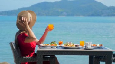 Tatilde olan genç bir kadın, şaşaalı bir deniz geçmişine sahip lüks bir tatil beldesi restoranında sabah kahvaltısının tadını çıkarıyor. Tropikal plajın dingin güzelliğinin tadını çıkarıyor..