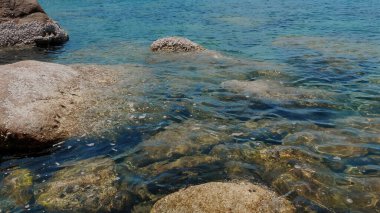 Turkuaz dalgalar pürüzsüz taşlara çarpıyor. Kıyı manzarasının güzelliği duyuları cezbeder. Seyahat ve yaz tatili kavramı.