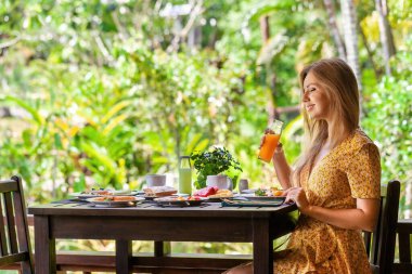 Masada oturan genç ve mutlu bir kadın ormanda lezzetli bir kahvaltı yapıyor. Lüks tatil beldesi ve tatil kavramı.