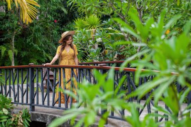 Uzun saçlı güzel bir kadın model yemyeşil bir bahçede tek başına duruyor. Tropik tatil.