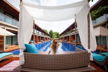 Yüzme havuzunun yanında güneşin tadını çıkaran beyaz elbiseli çekici bir kadın mankenin arka görüntüsü. Yaz zarafeti ve rahatlığı kavramı