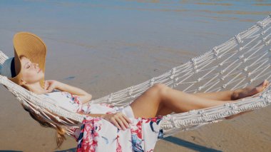 Deniz kenarındaki kumsalda hamakta uzanan rahat bir kadın. Tayland, Phuket Adası 'nda tatil. Ağır çekim. Plaj rahatlığı ve tropikal kaçamak kavramı.