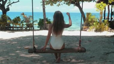 Tropik Tatil: Okyanus manzaralı bir tatil beldesinde salıncaktan hoşlanan bir kadın. Renkli bikinili, kumsalda sallanan esmer kız. Tasasız rahatlama ve özgürlük kavramı.