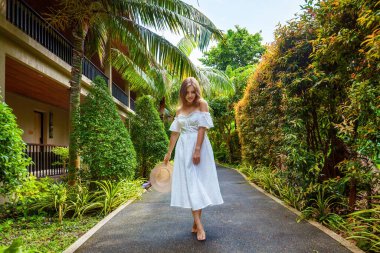 Tayland 'da yeşil tropikal ağaçların arasında yürüyen beyaz elbiseli bir kadın. Seyahat ve yaz tatili kavramı.