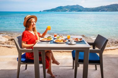 Lüks bir otelde dinlenen bir kadın, deniz manzaralı bir kahvaltı. Turkuaz okyanusa bakan tatilci kız. Tropikal tatil merkezleri..