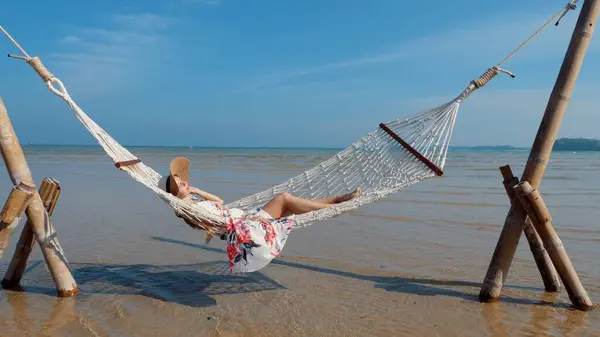 Young woman resting in hammock by the ocean. Vacation on Phuket island, Thailand. Concept of tranquil beach holiday and seaside serenity.