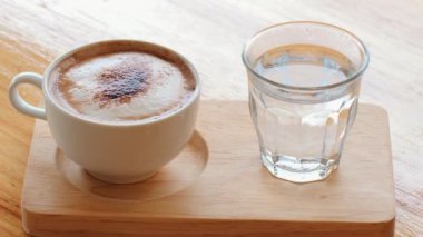 Kafe ahşap masada sıcak kapuçino ve kaynar su. Masa üstünde beyaz bardakta köpüklü latte. Kahve ve sabah. Kremalı sıcak kapuçino.