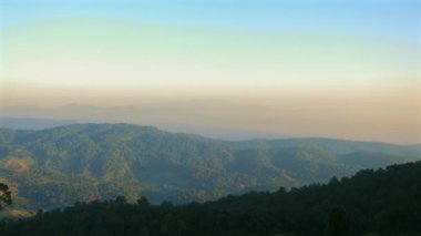 Görkemli dağ silueti, alevli günbatımı gökyüzüne karşı. Sis içinde dingin bir vadi, altın ışıkta. Doğal güzelliğin sakin bir sahnesi. Yürüyüş, kamp, rahatlama ve manzaranın tadını çıkarma..