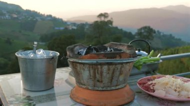Mangal ızgarasında cayır cayır yanan kömür, çarpıcı bir dağ günbatımına karşı hazırlanıyor. Lezzetli ve besleyici bir yemek için arka plan.
