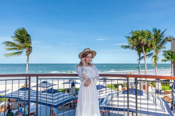 Side profile of woman wearing hat, overlooking tranquil sea and sandy shore. Beach vacation and peaceful retreat. Luxury resort lifestyle and tropical vacation.