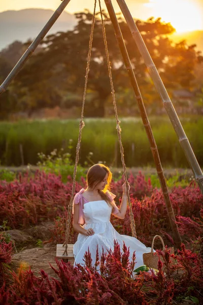 Woman in dress swings amid a sun-kissed flower field at sunset. Concept of Nature and Freedom in Summer