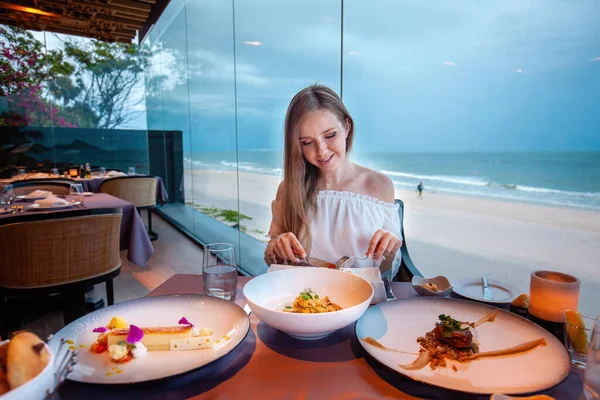 Young woman enjoying pasta dish in seaside restaurant, elegant dining with ocean view, luxurious travel lifestyle.