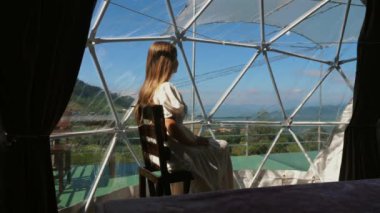 Şeffaf kamp çadırında oturan kadının arka görünüşü. Dağlık manzaraya bakan, göz kamaştırıcı bir deneyim. Eğlence gezisi ve eko-turizm.