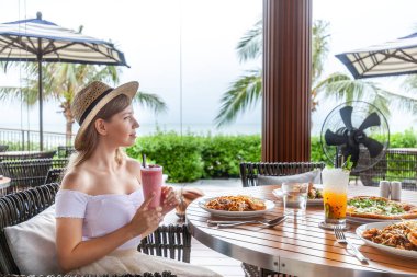 Plaj tatil köyü yemek deneyimi, kadın okyanus manzaralı kokteyl, rahat açık hava yemeği..