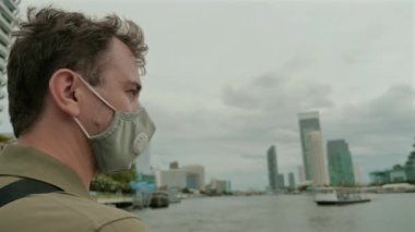 Nehir kenarını keşfederken maske takan bir adam. Kentsel seyahat ve sağlık güvenliği.