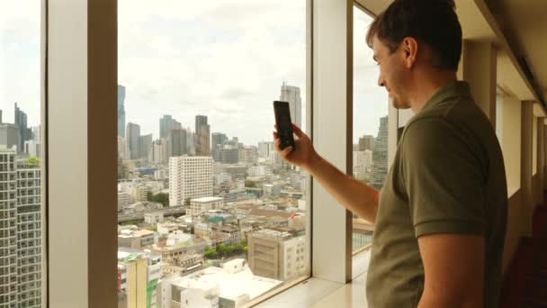 Man Using Smartphone Window Overlooking City Skyline Urban Lifestyle Technology — Stock Video