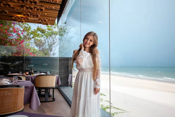 Sophisticated lady in elegant dress admires the calm seascape from a high-end eatery, a fusion of gourmet and nature. Gastronomy and relaxation.