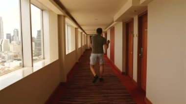 Şehir manzaralı otel koridorunda yürüyen eğlenceli bir adam. Seyahat ve konaklama.