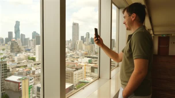 Homme Faisant Appel Vidéo Avec Smartphone Par Fenêtre Surplombant Ville — Video