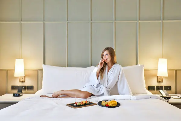 Woman enjoying luxury hotel room service with breakfast in bed. Hospitality and travel.