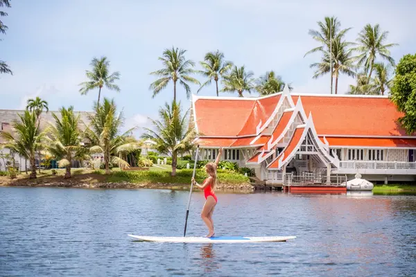 Woman paddleboarding on tranquil lake with tropical scenery. Water sports and leisure activity.