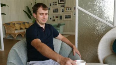 Rahat adam güneşli oturma odasında sabah kahvesinin tadını çıkarıyor. Ev konforu ve yaşam tarzı.