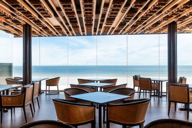 Ahşap masalar ve sandalyelerle çevrili, okyanus manzaralı, yerden tavana pencereli çağdaş bir kafeterya. Boş zaman ve seyahat.