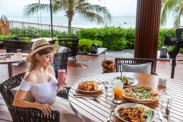 Elegant tourist savors exotic food, smoothie at sea view resort, leisure lifestyle and culinary experience.