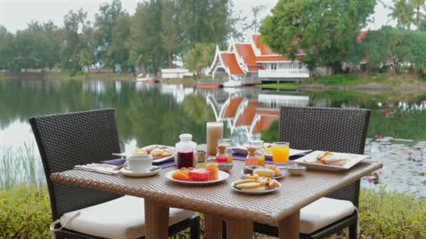 Tranquil Breakfast Setup Outdoor Resort View Serene Lake Traditional Architecture — Stockvideo