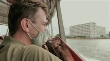 Yüzü maskeli bir adam tekneden şehir manzarası seyrediyor. Halk sağlığı ve güvenliği.