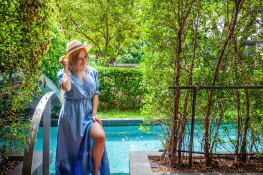 Tayland 'da sakin bir yüzme havuzunda poz veren şık şapkalı genç bir kadın. Cennette tatil, açık hava güzelliği ve tatil havası..