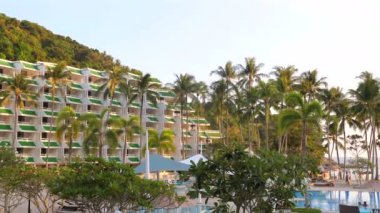 Önünde bereketli palmiye ağaçları ve tatil evleriyle dolu yamaçlarla çevrili büyük bir yüzme havuzu olan tropik bir tatil oteli. Seyahat ve lüks konaklama.