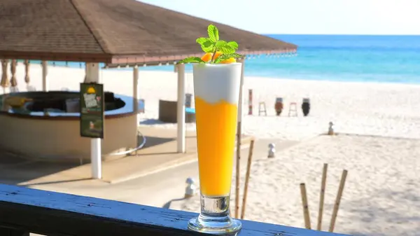 Refreshing tropical cocktail on beachside bar counter with pristine sandy beach and ocean view in background. Vacation and travel relaxation.