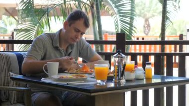 Kızgın üzgün adam tropikal tatil köyünde çeşitli yiyecek ve içeceklerle birlikte kahvaltıda. Tatil ve tatil..