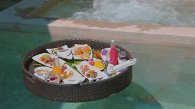 Lüks tatil beldesi kahvaltısı sonsuz havuzda yüzen tepside sunuluyor, egzotik tatil ortamlarında çeşitli meyve, ekmek ve içecekler sunuluyor. Tropik tatil ve yemek zarafeti.
