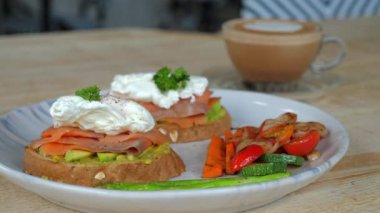 Avokado tostunda haşlanmış yumurta, füme somon ve kapuçino ile servis edilen ızgara sebzeli gurme kahvaltısı. Sağlıklı ve besleyici sabah yemeği.